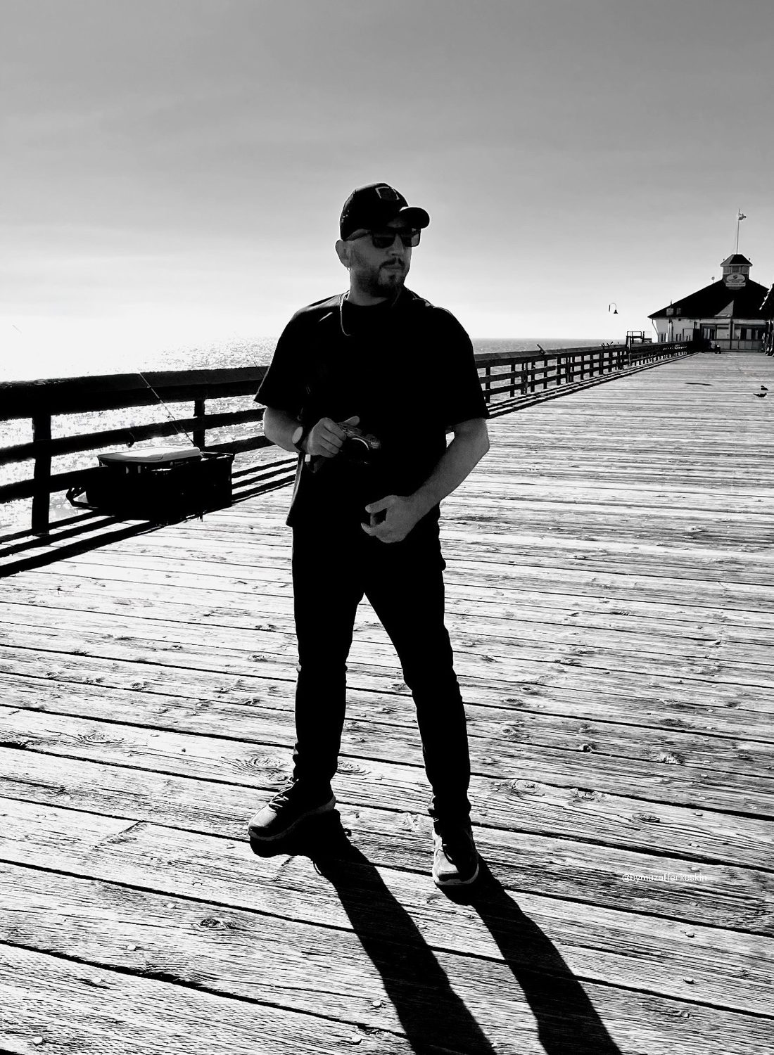 Muzaffer Keskin on a wooden pier holding a camera, black and white